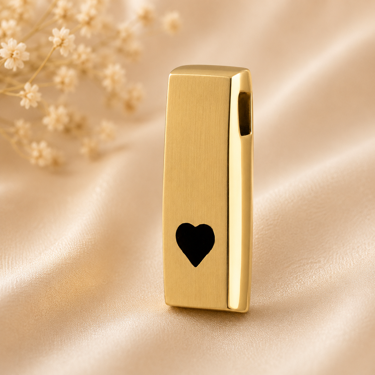 14 karaat gouden ashanger met zwart hartdetail op zachte champagnekleurige satijnen achtergrond – stijlvol herinneringssieraad voor een symbolische hoeveelheid as.