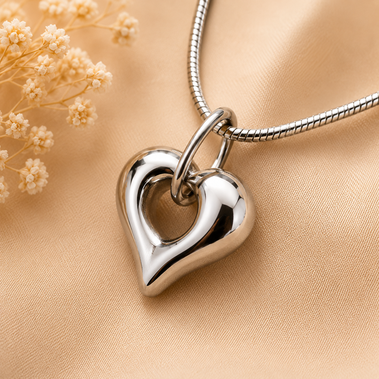 Zilverkleurig assieraad in open hartvorm aan slangencollier op warme beige achtergrond – elegant herinneringssieraad als symbool van liefde, verbondenheid en een blijvende herinnering aan een dierbare.
