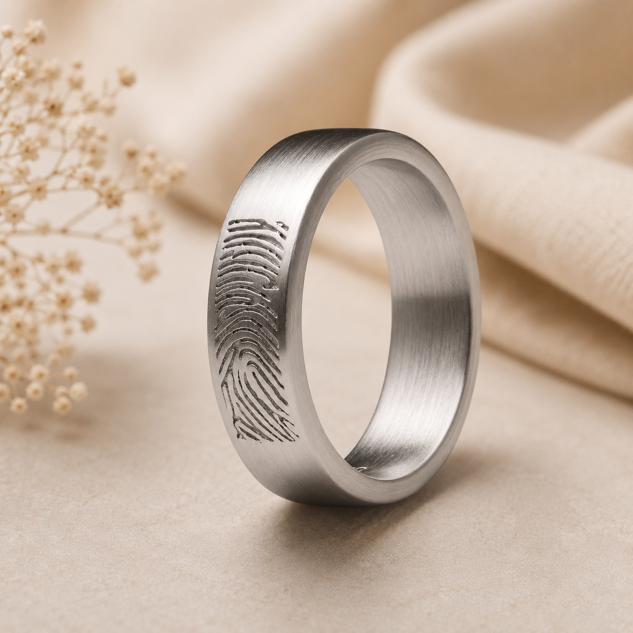 Matte zilveren herinneringsring met gegraveerde vingerafdruk op een zachte beige achtergrond, een stijlvol en persoonlijk sieraad vol betekenis.