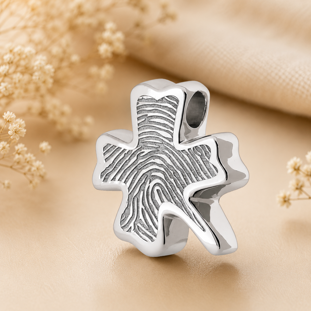 925 sterling zilveren assieraad in klavervorm met subtiele vingerafdruk gravure op warme beige achtergrond – stijlvol herinneringssieraad als symbool van liefde, verbondenheid en een blijvende herinnering aan een dierbare.
