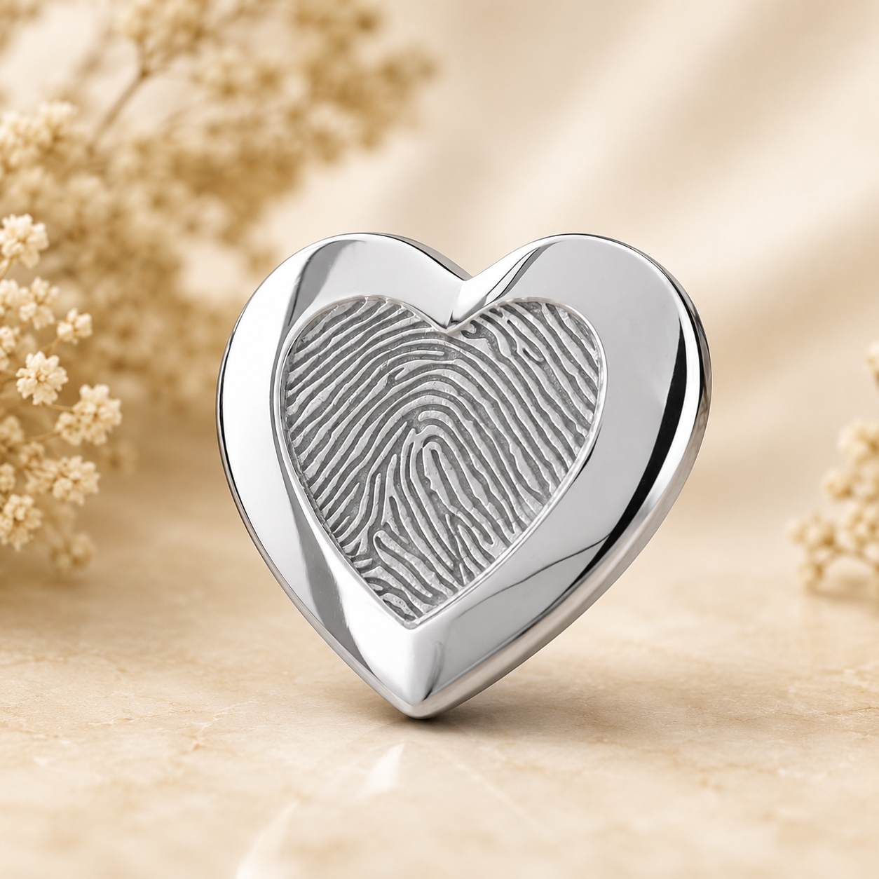 925 sterling zilveren assieraad in hartvorm met subtiele vingerafdruk gravure op warme beige achtergrond – stijlvol herinneringssieraad als tastbare herinnering aan een dierbare.